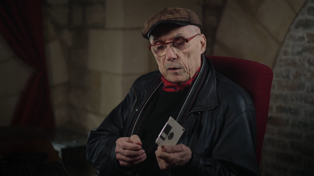 Capture d'écran du film La découverte de la chouette d'or. On y voit Michel Becker assis, tenant la disquette.